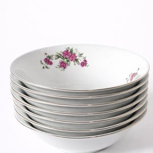 以下が含まれることがあります： 白い磁器のボウルが6つ重ねられています。各ボウルは金色の縁取りと、緑の葉を持つピンクの花のクラスターが特徴です。ボウルは互いの上に積み重ねられています。