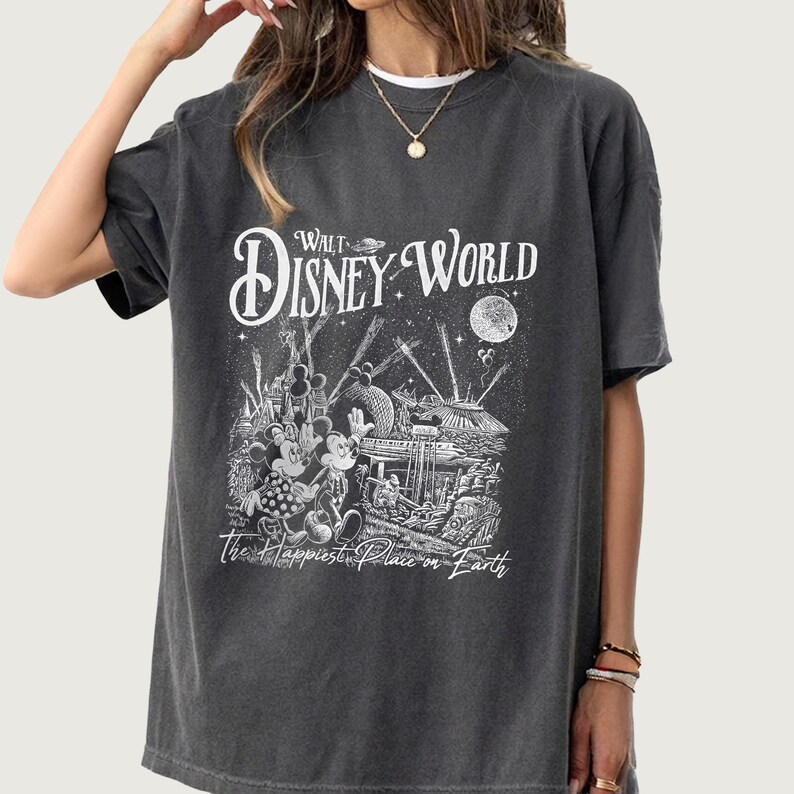 May include: Dark gray t-shirt featuring a black and white graphic of Mickey and Minnie Mouse in front of a Disney World scene. The text "Walt Disney World" and "The Happiest Place on Earth" are also displayed on the shirt.
