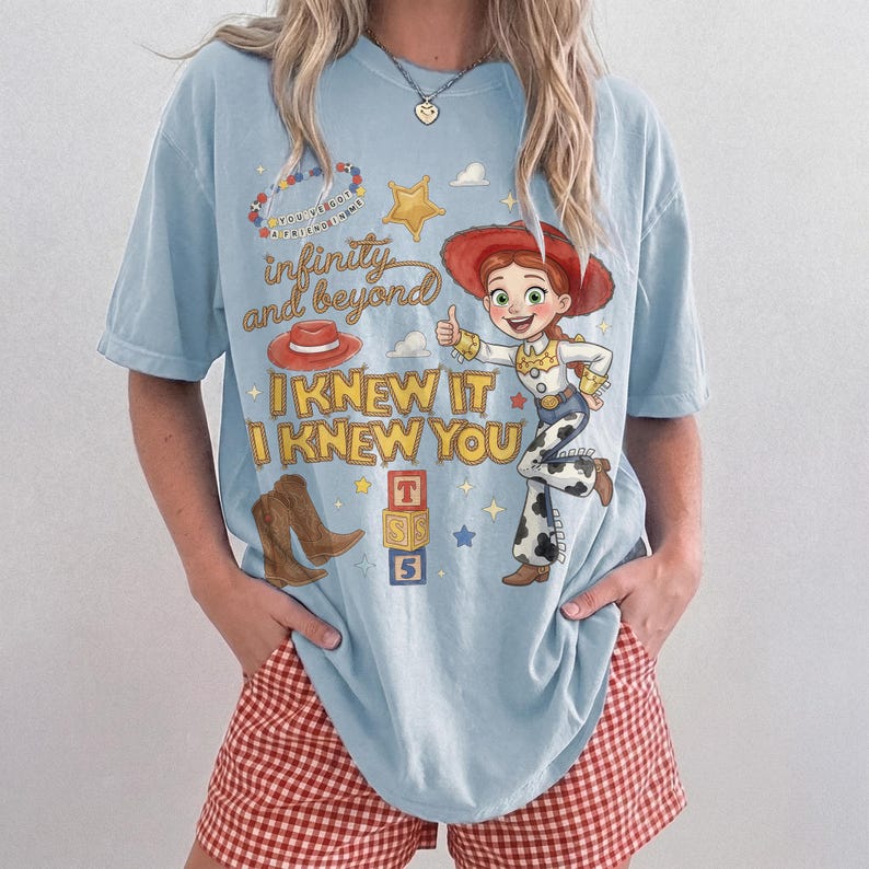 Może przedstawiać: Jasnoniebieski t-shirt z kr&oacute;tkim rękawem z nadrukiem graficznym przedstawiającym postać kowbojki, czerwony kapelusz, brązowe buty i klocki z literami. Tekst głosi "infinity and beyond", "I KNEW IT I KNEW YOU" oraz "YOU'VE GOT A FRIEND IN ME".