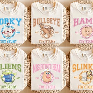 Pu&ograve; includere: Sei magliette color crema con personaggi di Toy Story: Forky, Bullseye, Hamm, Aliens, Mrs. Potato Head e Slinky. Ogni maglietta presenta il nome del personaggio, il testo "EST. 1995" e "TOY STORY" sotto.