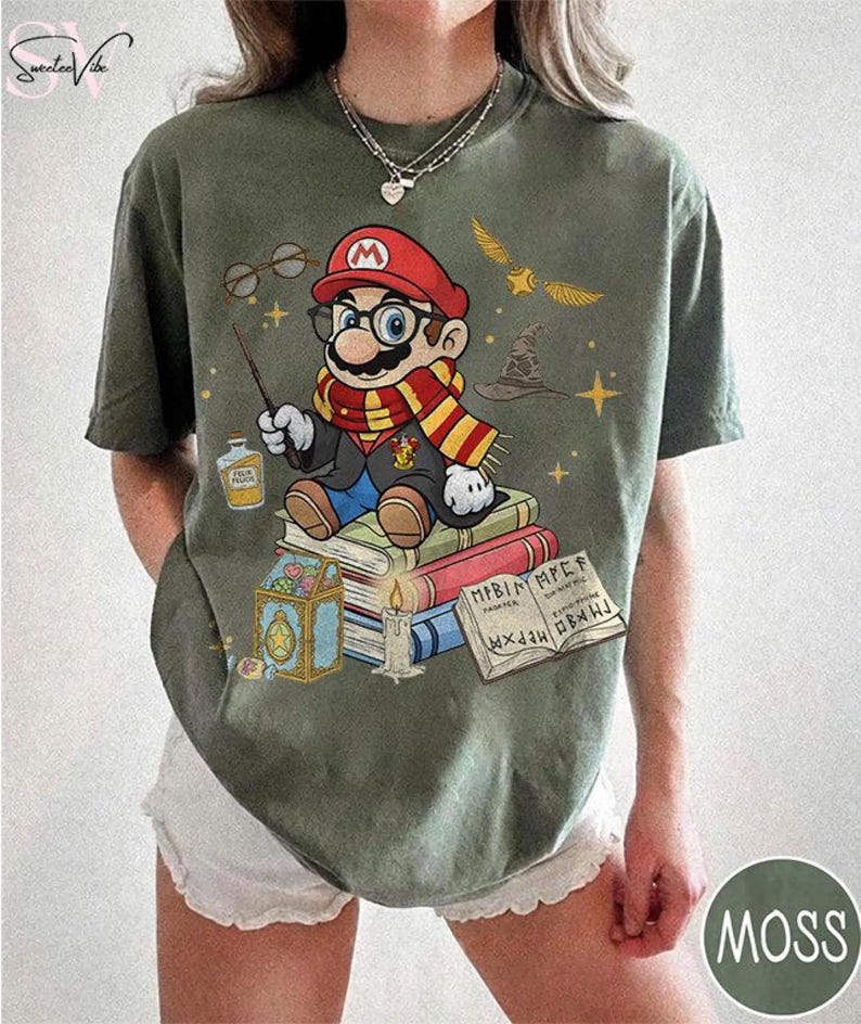 May include: Moss green t-shirt featuring a cartoon Mario character dressed as a wizard, sitting on books. The design includes a wand, glasses, a scarf, and a wizard hat. The shirt has the word "MOSS" in a circle on the bottom right.
