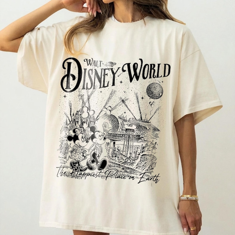 May include: Cream-colored t-shirt featuring a black and white graphic of Mickey and Minnie Mouse in front of a Walt Disney World scene. The text "Walt Disney World" and "The Happiest Place on Earth" are also printed on the shirt.