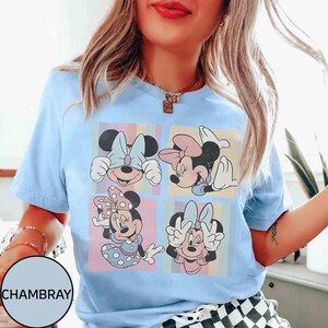 May include: Pale blue t-shirt with a graphic of Minnie Mouse in four panels. Each panel shows a different pose of Minnie against a pastel background. The shirt has a round neck and short sleeves.