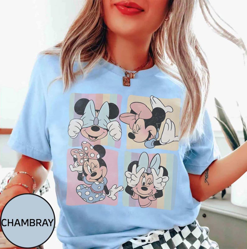 May include: Pale blue t-shirt with a graphic of Minnie Mouse in four panels. Each panel shows a different pose of Minnie against a pastel background. The shirt has a round neck and short sleeves.