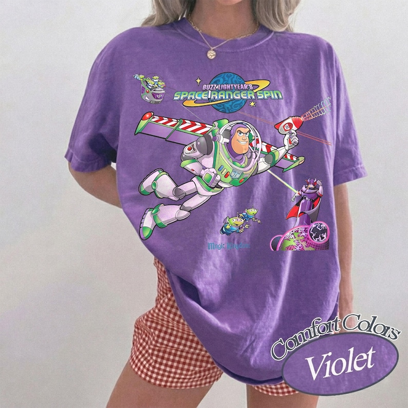 May include: A purple t-shirt featuring a graphic of Buzz Lightyear from Space Ranger Spin. The design includes Buzz Lightyear in his white, green, and purple suit, a planet, and the text Buzz Lightyear's Space Ranger Spin. The shirt has a crew neck.