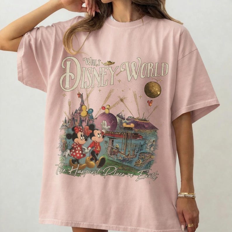 May include: Light pink t-shirt featuring a vintage-style Walt Disney World graphic. The design includes Mickey and Minnie Mouse, a castle, and the phrase "The Happiest Place on Earth."