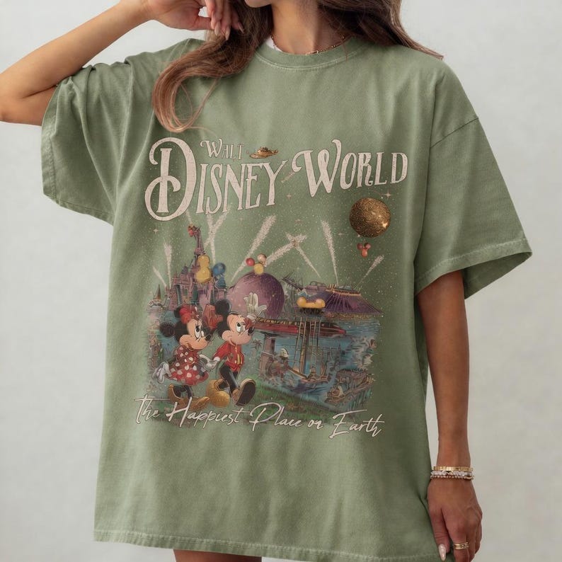 May include: Olive green t-shirt featuring a vintage-style graphic of Mickey and Minnie Mouse at Walt Disney World. The design includes the text "Walt Disney World" and "The Happiest Place on Earth."