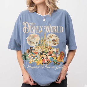 May include: A light blue t-shirt featuring a graphic of Disney characters and the text "Walt Disney World" and "The Happiest Place on Earth". The graphic includes Mickey Mouse, Donald Duck, and other characters.