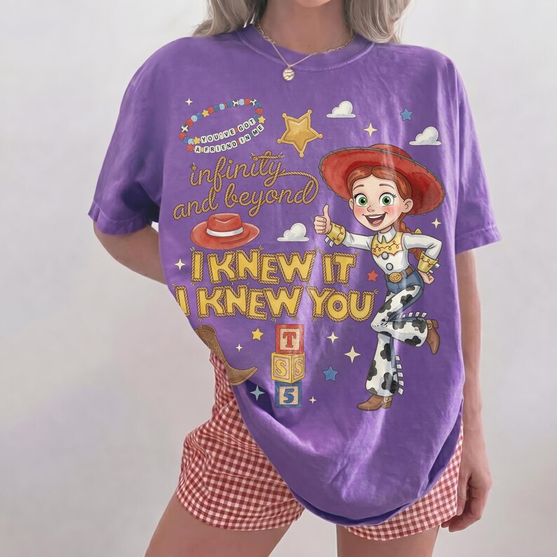 Może przedstawiać: Fioletowy t-shirt z grafiką przedstawiającą kowbojkę z rudymi włosami w kapeluszu oraz napisy "You've got a friend in me", "infinity and beyond" i "I KNEW IT I KNEW YOU", wraz z ilustracjami czerwonego kapelusza, gwiazdy i klock&oacute;w z literami.