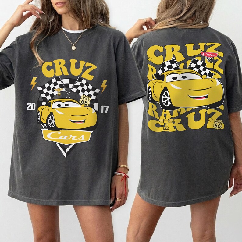 May include: Dark grey t-shirt with a yellow cartoon car design and the word "CRUZ" and "Cars". The front has lightning bolts, chequered flags, and the numbers "20" and "17". The back of the shirt also features the yellow car and the text "CRUZ".