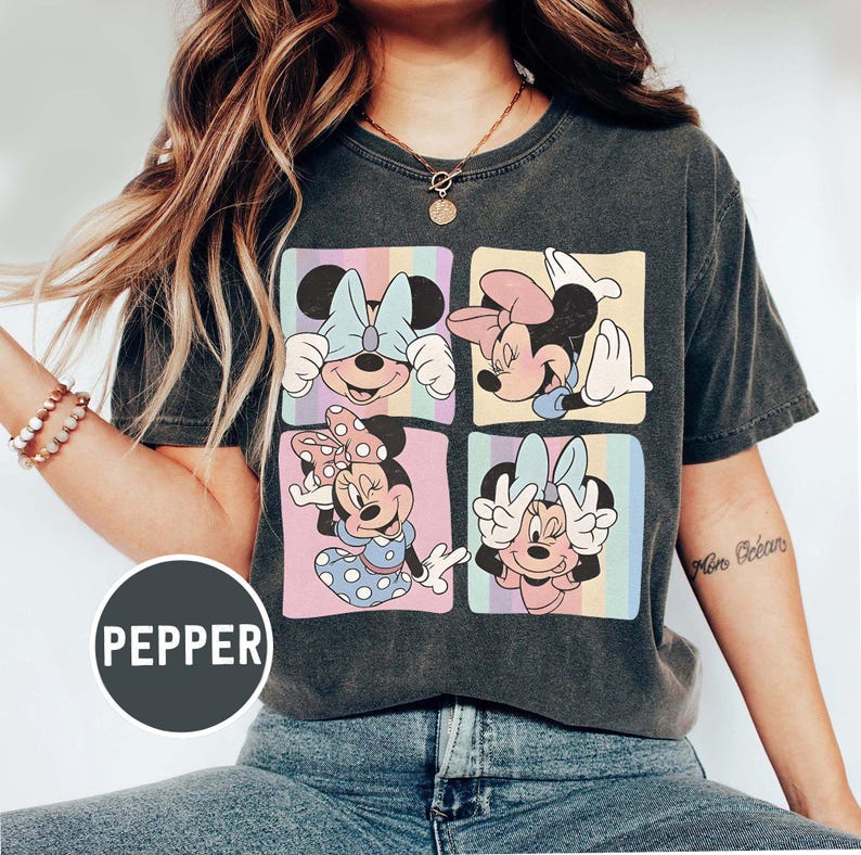 May include: Dark grey t-shirt with a four-panel design of Minnie Mouse in different poses. Each panel has a pastel rainbow background. The word "PEPPER" is printed on a circular label at the bottom.