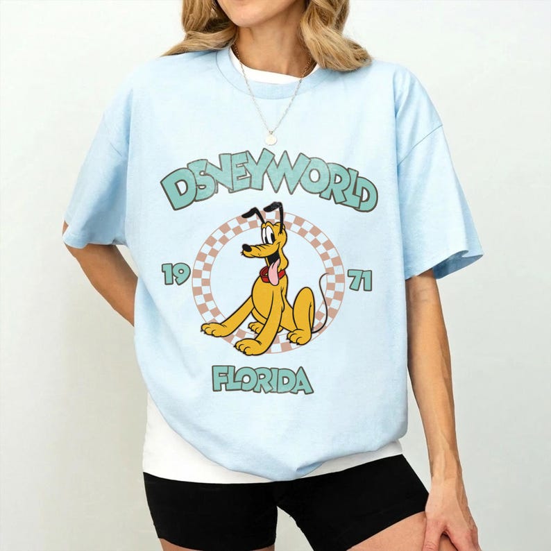 May include: Light blue t-shirt with a vintage Disney World graphic. The design features Pluto, the text "Disney World 1971 Florida", and a checkered circle. The shirt has short sleeves and a crew neck.