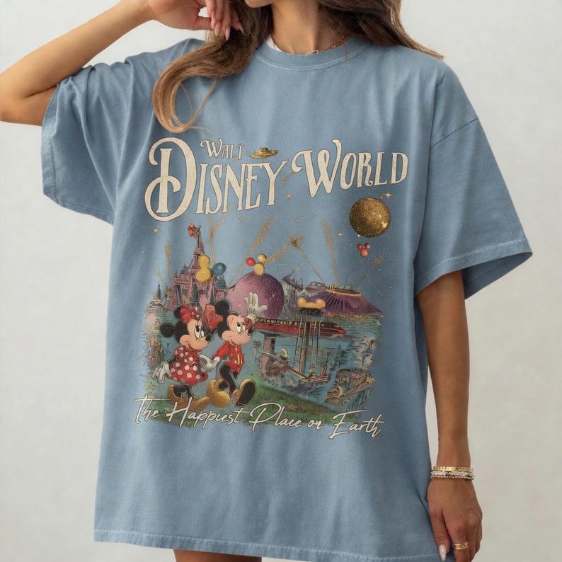 May include: Light blue t-shirt featuring a vintage-style Walt Disney World graphic. The design includes Mickey and Minnie Mouse, a castle, and the phrase "The Happiest Place on Earth."