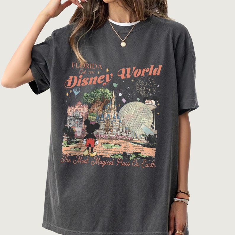 May include: Dark gray t-shirt featuring a colorful graphic of Disney World landmarks, including Cinderella's castle, Spaceship Earth, and Mickey Mouse. The text reads "Florida Disney World" and "The Most Magical Place On Earth."