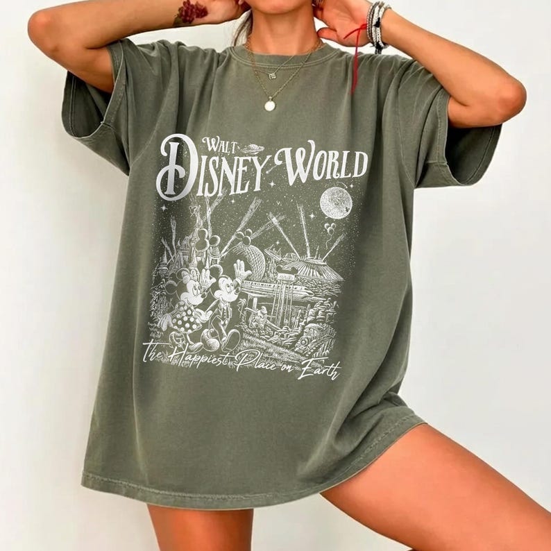 May include: Olive green t-shirt featuring a graphic of Mickey and Minnie Mouse at Walt Disney World. The design includes the words "Walt Disney World" and "The Happiest Place on Earth" in white lettering. The shirt has short sleeves and a relaxed fit.