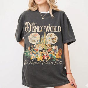 May include: Dark gray t-shirt featuring a colorful graphic of Disney characters and the text "Walt Disney World" and "The Happiest Place on Earth." The design includes Mickey Mouse, Donald Duck, and other beloved characters.