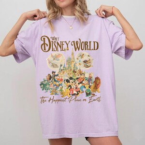 May include: A light purple t-shirt featuring a Walt Disney World graphic. The design includes the words "Walt Disney World" in a gold script, along with illustrations of Disney characters and the phrase "The Happiest Place on Earth."