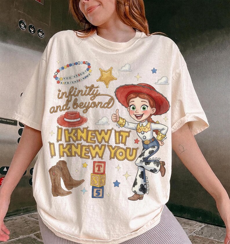 Może przedstawiać: Kremowy t-shirt z grafiką przedstawiającą kowbojkę, czerwony kapelusz, brązowe kowbojki i klocki z literami. Napis głosi "infinity and beyond" oraz "I KNEW IT I KNEW YOU", a całość uzupełnia grafika przedstawiająca naszyjnik z koralik&oacute;w.