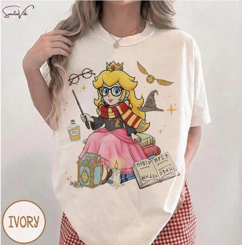 May include: Ivory-colored t-shirt featuring a cartoon princess with glasses, a wand, and a scarf, styled in a Harry Potter theme. The design includes a golden snitch, a sorting hat, and a potion bottle. The shirt has the word "IVORY" printed on it.