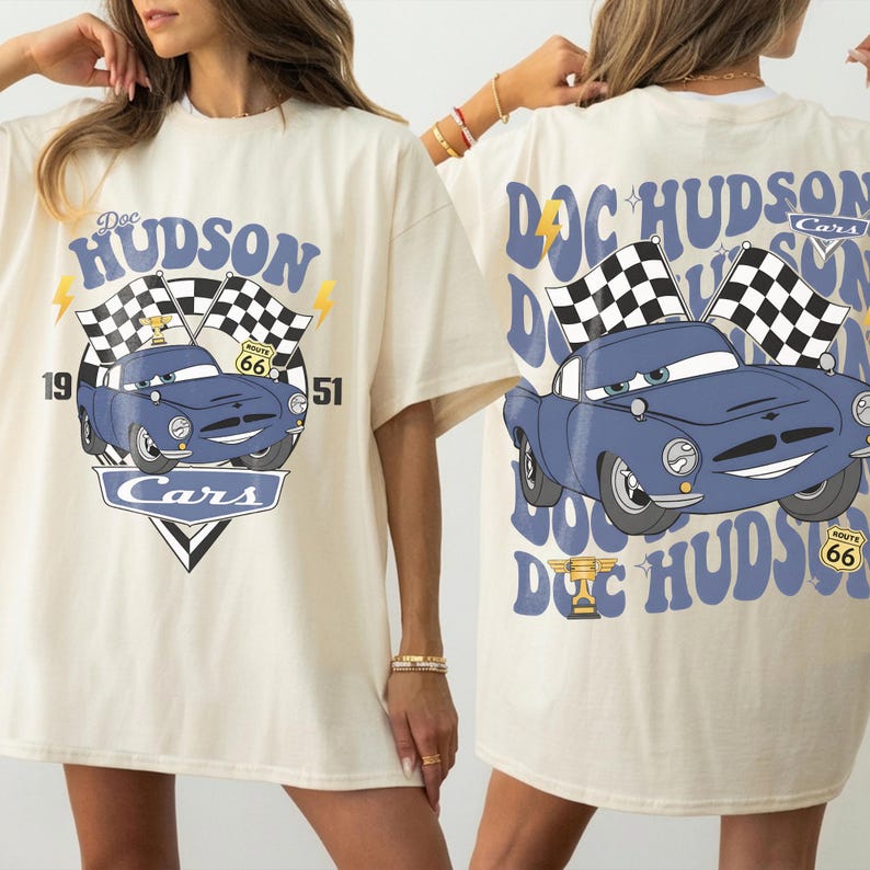 May include: Cream-coloured t-shirt with a blue cartoon car design, checkered flags, and the text "Doc Hudson Cars". The front design includes the years "19" and "51" and the Route 66 logo. The back of the shirt also features the car and text.