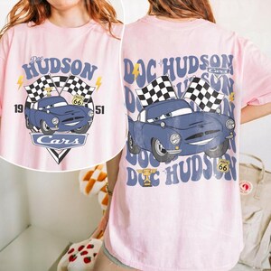 May include: A white ceramic mug with a black handle and the text "But First, Coffee" in a black, handwritten-style font. The mug is on a white surface.