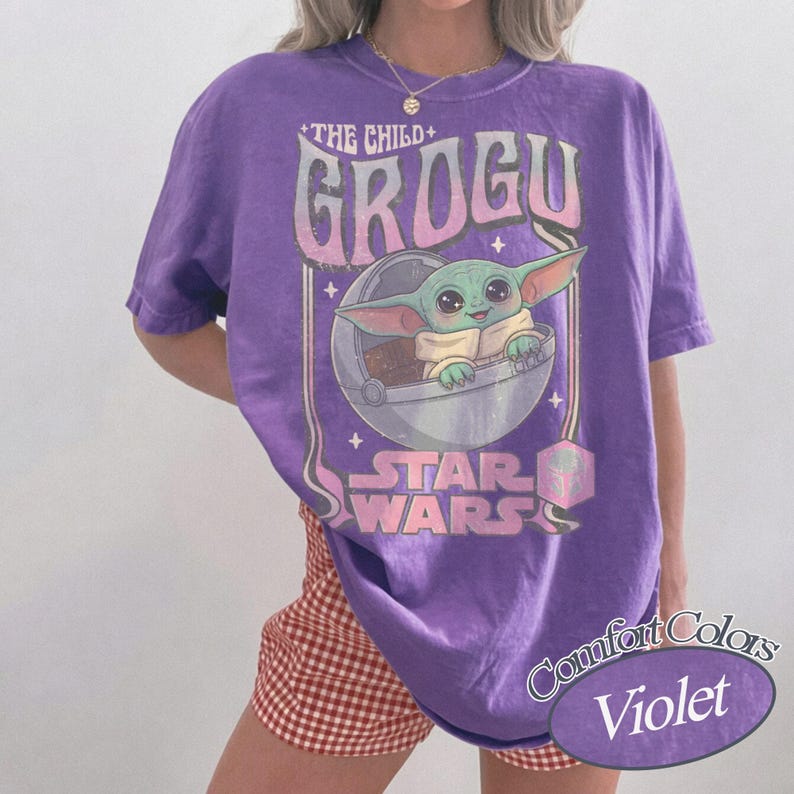 Puede incluir: Camiseta violeta Comfort Colors con Grogu de Star Wars. El gr&aacute;fico incluye el texto "THE CHILD + GROGU" y una imagen de Grogu en una c&aacute;psula. La camiseta es de corte holgado.