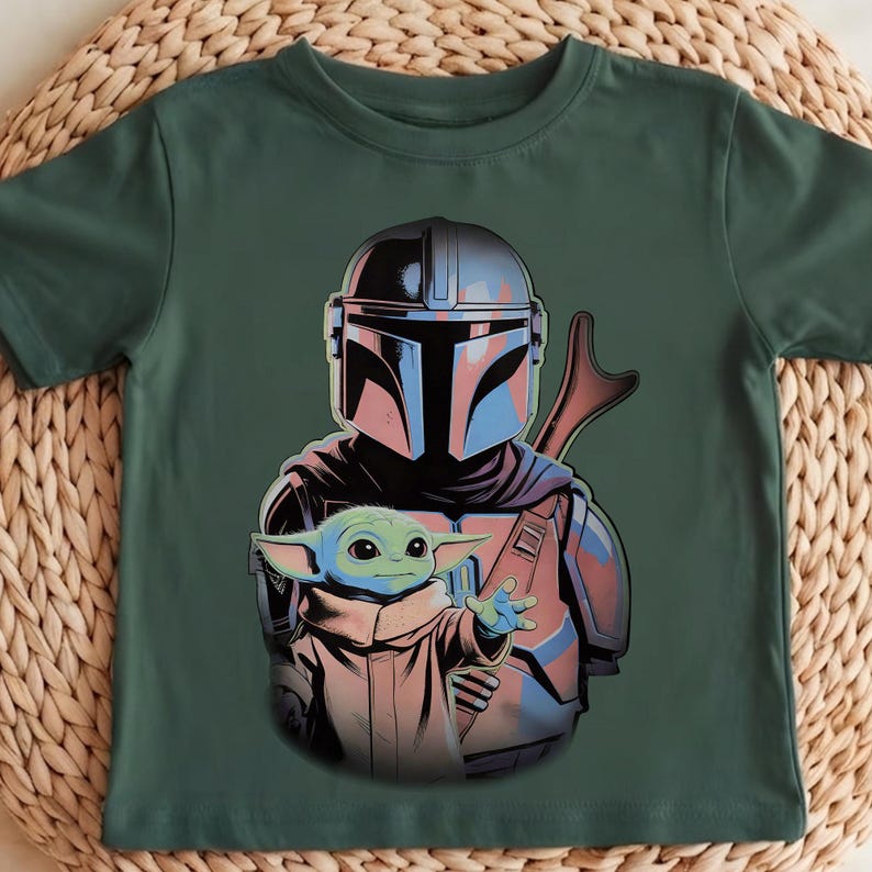 K&ouml;nnte beinhalten: Ein dunkelgr&uuml;nes Kurzarm-T-Shirt mit einem Grafikdruck eines Charakters, der einen metallisch silbernen Helm und eine R&uuml;stung tr&auml;gt und hinter einer kleinen gr&uuml;nen Kreatur mit gro&szlig;en Ohren in einer beigen Robe steht.