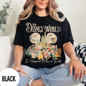 May include: Black t-shirt featuring a Walt Disney World design. The shirt displays the words "Walt Disney World" in gold lettering above a graphic of Disney characters and Cinderella's castle. The text "The Happiest Place on Earth" is below the graphic.