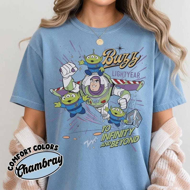 May include: Light blue t-shirt featuring Buzz Lightyear and the Little Green Men from Toy Story. The graphic includes the text "Buzz Lightyear" and "To Infinity and Beyond". The shirt is labeled "Comfort Colors Chambray".