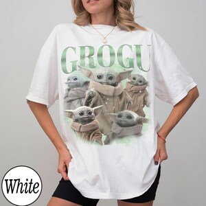 May include: White t-shirt featuring a graphic of Grogu, also known as Baby Yoda, from The Mandalorian. The word "GROGU" is printed in green above the image of Grogu. The t-shirt is a casual, oversized style.