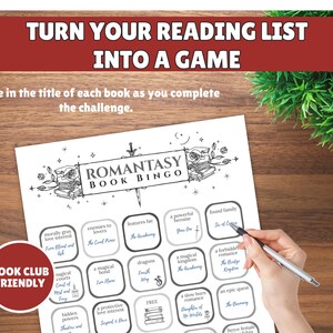May include: A black and white Romantasy Book Bingo game sheet with a pen. The sheet has a red and white "Book Club Friendly" logo. The text on the sheet includes "Turn Your Reading List Into A Game" and "Romantasy Book Bingo".