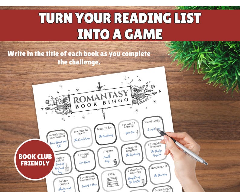 May include: A black and white Romantasy Book Bingo game sheet with a pen. The sheet has a red and white "Book Club Friendly" logo. The text on the sheet includes "Turn Your Reading List Into A Game" and "Romantasy Book Bingo".