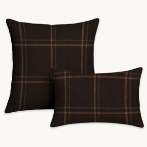May include: A square throw pillow and a rectangular throw pillow, both featuring a dark brown fabric with a subtle grid pattern composed of thin, intersecting light brown and grey lines that create a classic plaid design across the surfaces.