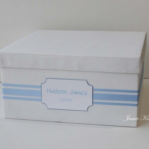 May include: White keepsake box with blue stripes and a label that reads "Hudson James 5.09.15".