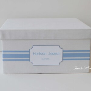May include: White keepsake box with a blue and white striped ribbon and a label that reads "Hudson James 5.09.15".