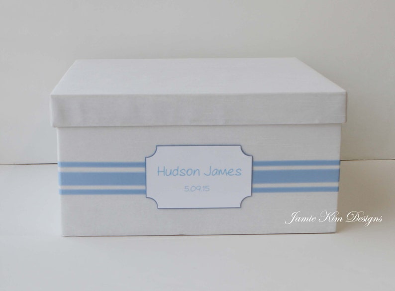 May include: White keepsake box with a blue and white striped ribbon and a label that reads "Hudson James 5.09.15".