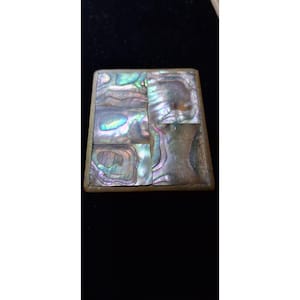 May include: A square, iridescent abalone shell box with a brass-colored frame. The shell is divided into six sections, displaying shades of blue, green, and purple. The box is set against a dark background.