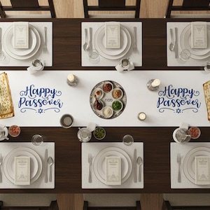 Op de afbeelding: Overzicht van een Pesach Seder-tafelsetting. De donkere houten tafel is gedekt voor acht gasten met witte placemats, borden en bestek. Een witte loper toont "Happy Passover" in blauw schrift. Een Seder-bord en matzah zijn ook aanwezig.