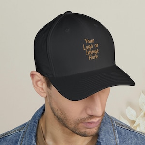May include: A black baseball cap featuring the embroidered text Your Logo or Image Here in a gold-colored thread on the front panel. The cap has a structured crown, a curved brim, and stitched eyelets for ventilation on the top panels.