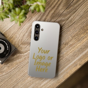 May include: A light gray smartphone case featuring a vertical camera array with three lenses and a flash. The back of the case displays the gold-colored text "Your Logo or Image Here" in a script font, positioned centrally below the camera module.