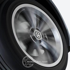 Peut inclure: Gros plan d'une roue de voiture en mouvement. La roue a une jante argentée et un pneu noir. Le centre de la roue présente le logo Volkswagen. L'image a un effet flou, suggérant le mouvement. Le texte "WHEELSFLOAT" est en bas.