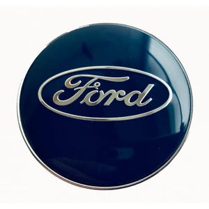 Puede incluir: Un emblema Ford azul marino con el logotipo Ford plateado en forma ovalada. El emblema tiene una superficie brillante y un borde plateado.