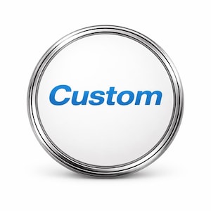 May include: A circular button with a metallic silver rim and a white center. The word Custom is printed in a bold blue sans-serif font across the middle of the white surface. The design features a clean, high-contrast look with a smooth finish.