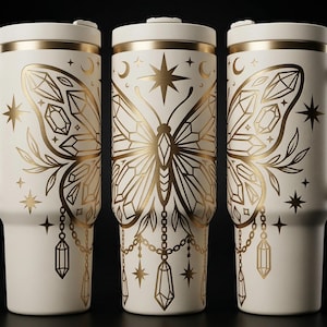 Puede incluir: Taza de viaje blanquecina con un diseño de mariposa dorada. Las alas de la mariposa están detalladas con formas geométricas y acentos celestiales. La taza tiene un asa y una tapa, y está decorada con estrellas, lunas y cristales.