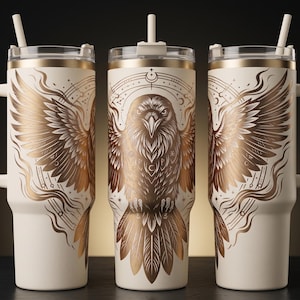 Puede incluir: Tres tazas de viaje de color crema con diseños dorados de águilas y alas. Cada taza tiene un asa, una tapa transparente y una pajita. El águila está centrada en una taza, mientras que las alas aparecen en las otras dos. Las tazas son cilíndricas y parecen estar aisladas.