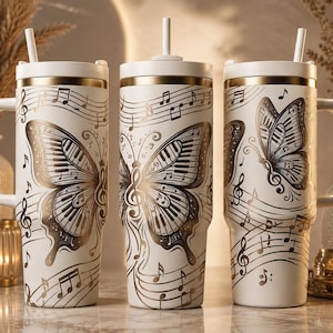 Puede incluir: Tres vasos blancos con asas y pajitas, con un diseño de mariposa en tono dorado donde las alas están compuestas por teclas de piano. Notas musicales y pentagramas están impresos en la superficie, con un borde dorado en la parte superior de cada vaso.