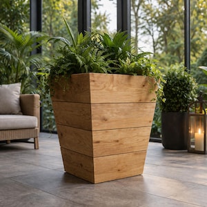 May include: A large, wooden planter box filled with lush green plants. The planter has a trapezoidal shape, constructed from horizontal wooden planks. The natural wood color complements the greenery, creating a stylish outdoor decor element.