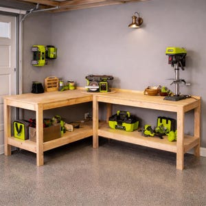 May include: A wooden workbench with various power tools and accessories. The tools are mainly lime green and black. The workbench is in a garage setting with a grey wall and concrete floor.