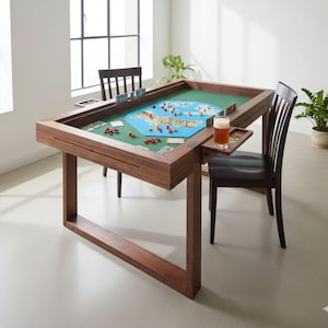 May include: A wooden game table with a green felt playing surface and a blue game board. The table has a built-in tray and is surrounded by two chairs. A glass of beer sits on the tray. The table is in a well-lit room.