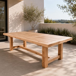 Puede incluir: Una mesa de comedor rectangular para exteriores fabricada en madera natural de tono claro. El tablero presenta un diseño de listones con vetas de madera visibles, sostenido por cuatro patas cuadradas robustas unidas por un marco base.